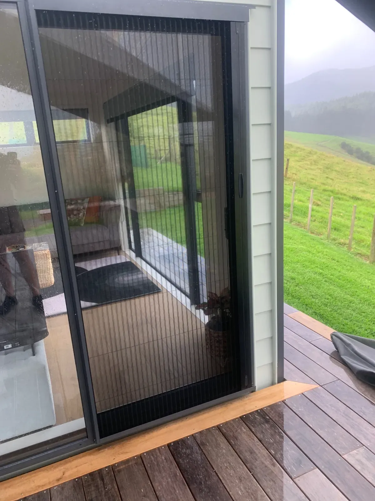 Brio folding screen on a tiny-home door, opening to a misty Coromandel deck and hills