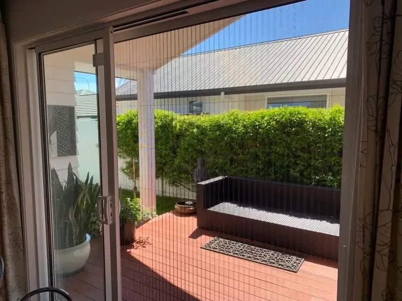 Brio pleated screen spanning a corner stacker opening onto a red deck at Papamoa