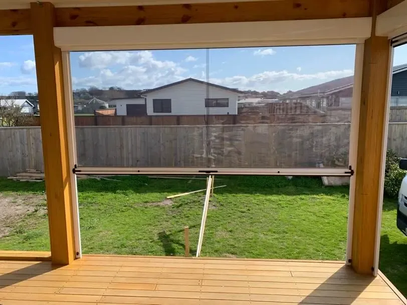 Ziptrak outdoor blind part-lowered between the posts of a timber pergola at Waiotahe
