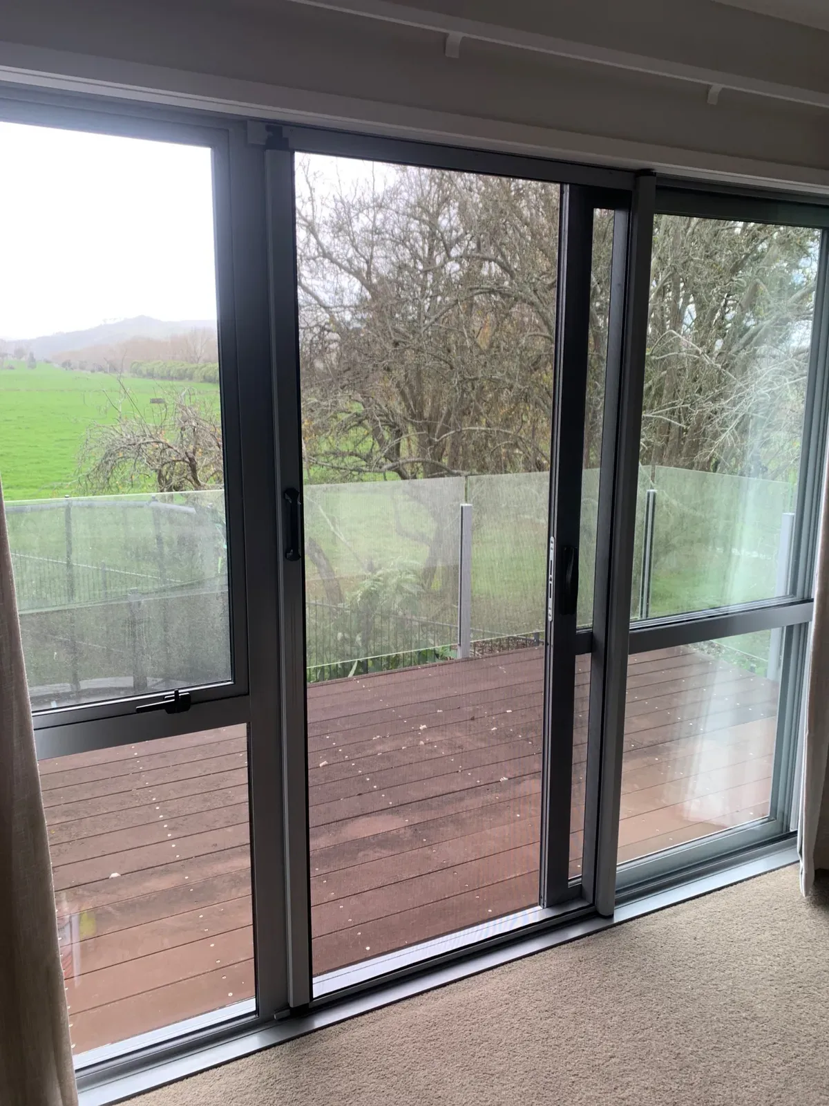 MeshLock screen on a ranch slider opening to a glass-balustrade deck and rural Waikato paddocks