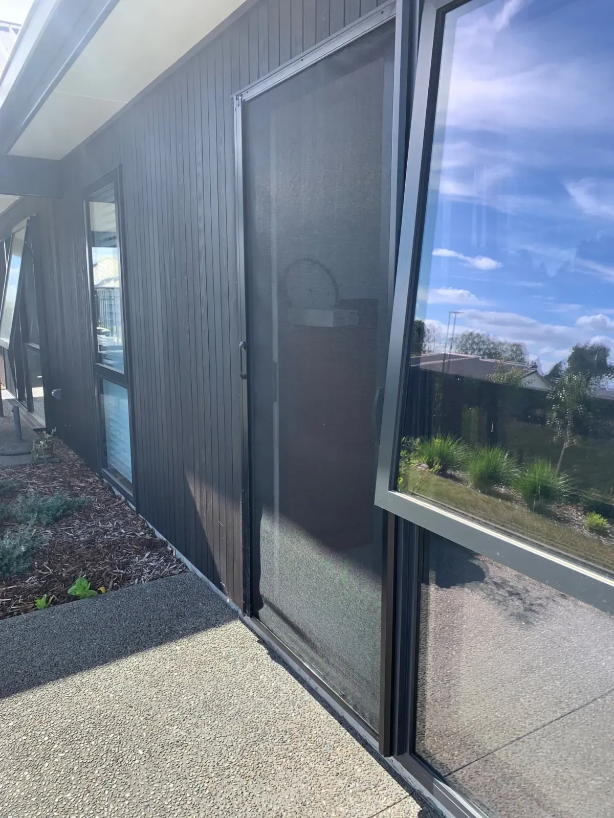 Matt Black MeshLock screen on dark cladding, sky reflected in the glass, Morrinsville