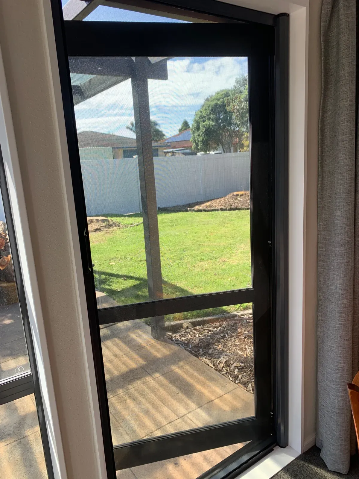 MeshLock retractable door screen drawn across a sliding door, opening to a green lawn and white fence
