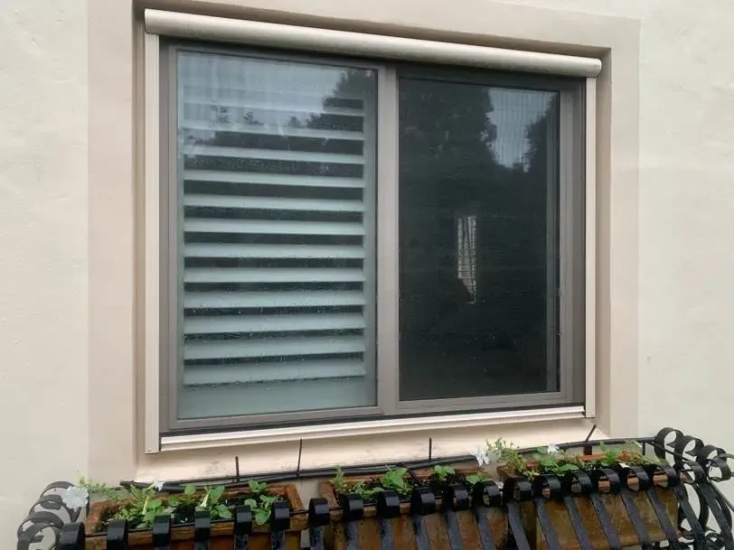 Serene screen and housing on a bedroom window above a planted window box, formal garden beyond
