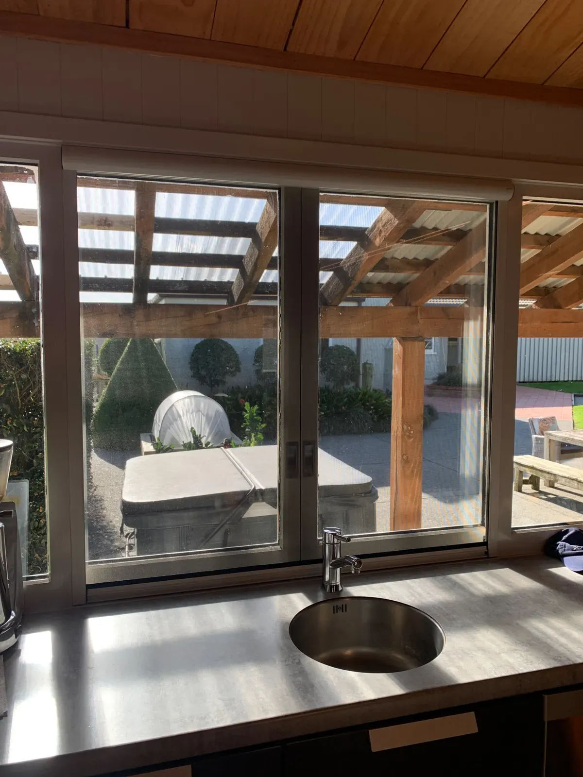 Serene window screen above a kitchen sink, framing a timber pergola and courtyard garden