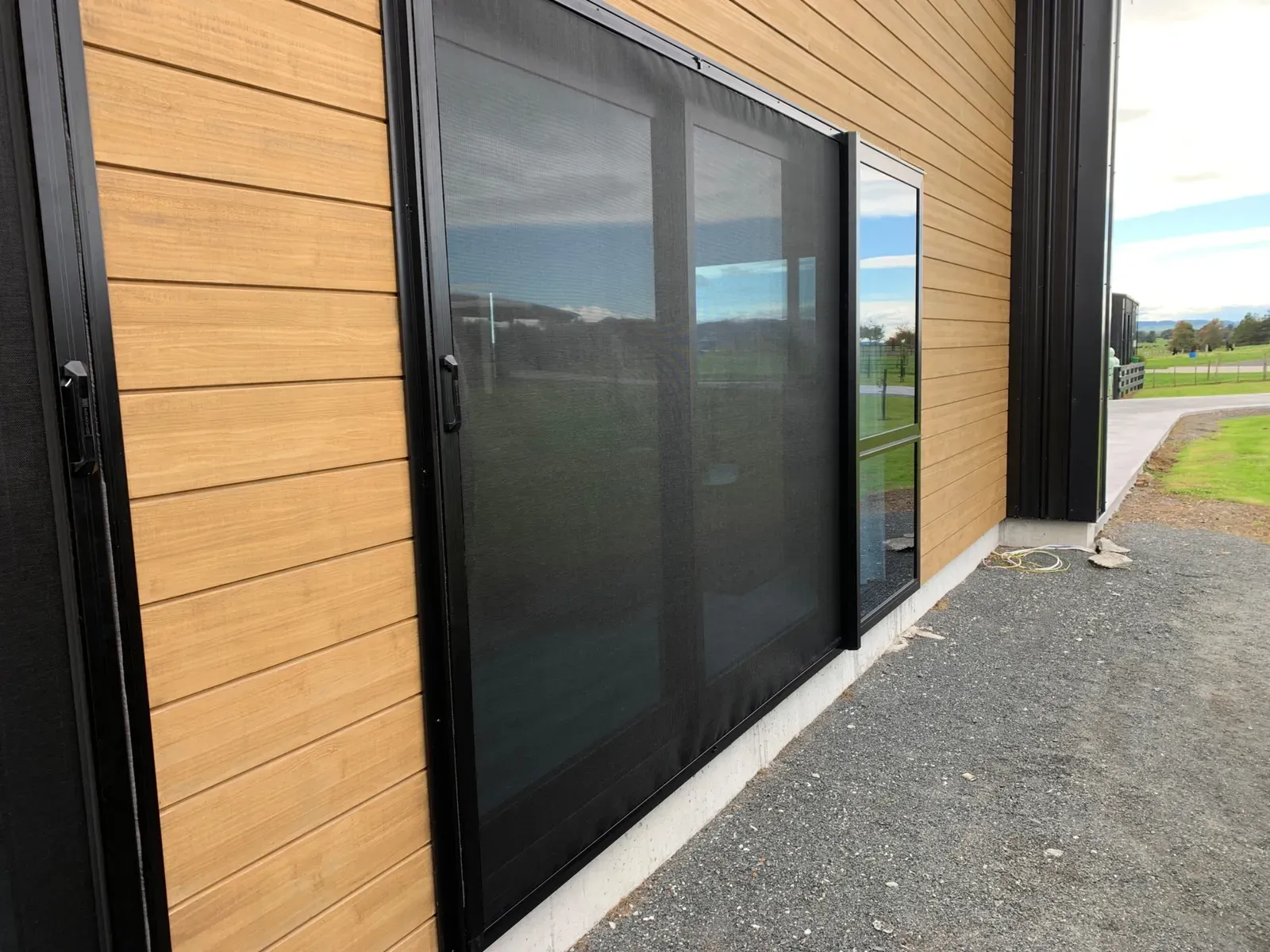 Retractable Wall Screen on cedar-clad sliders at a rural Morrinsville home