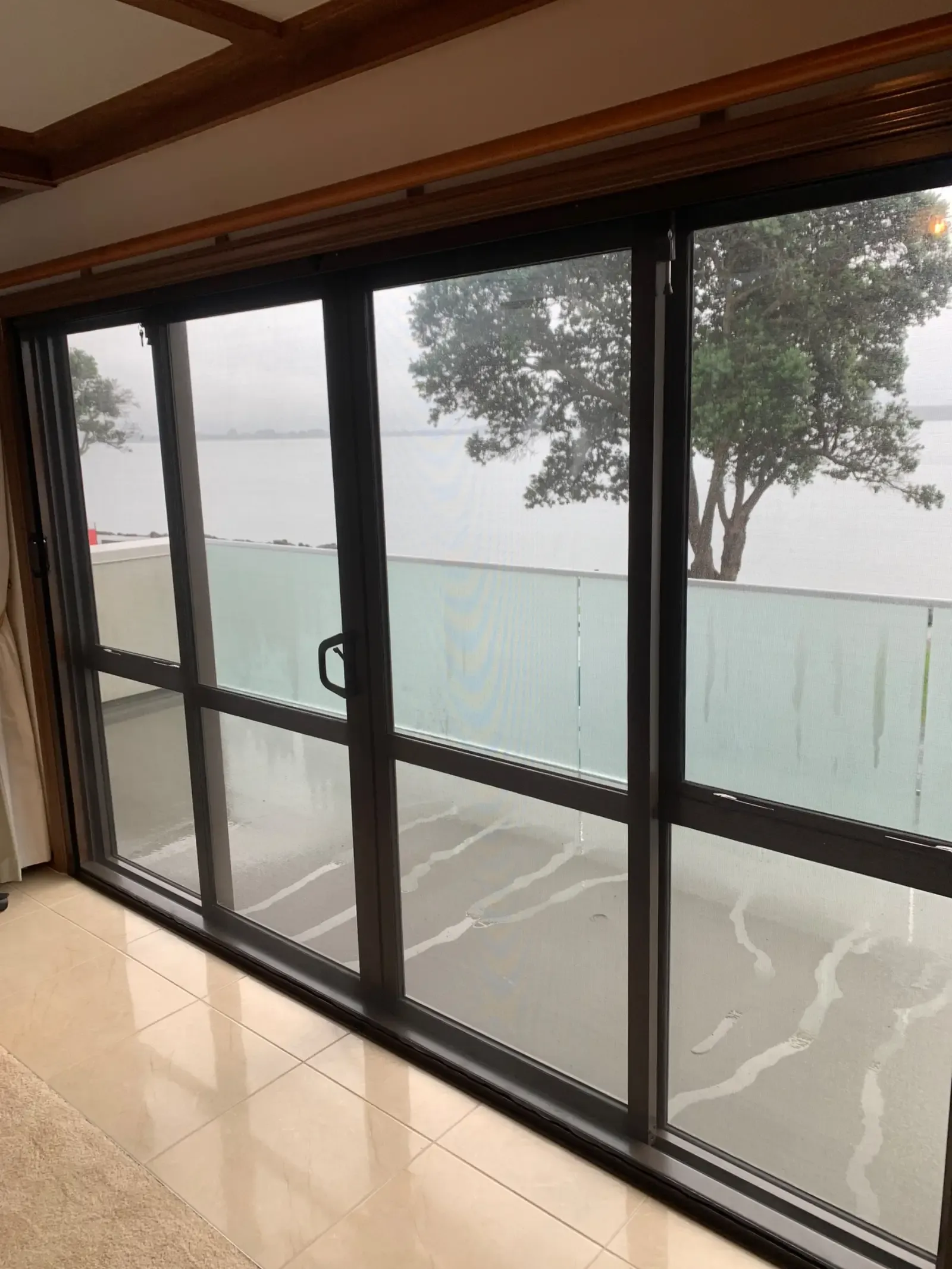 Retractable Wall Screen drawn across a balcony slider, tidal harbour and pōhutukawa beyond
