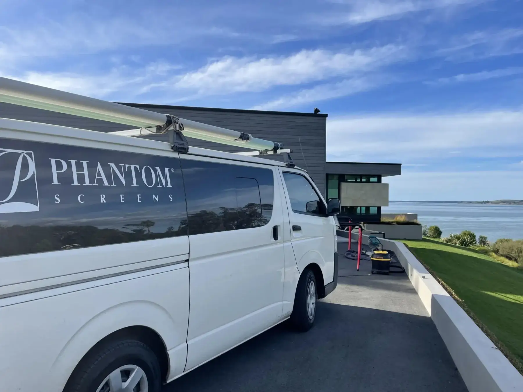 A Phantom Screens van at a modern coastal home on install day, overlooking a Tauranga harbour