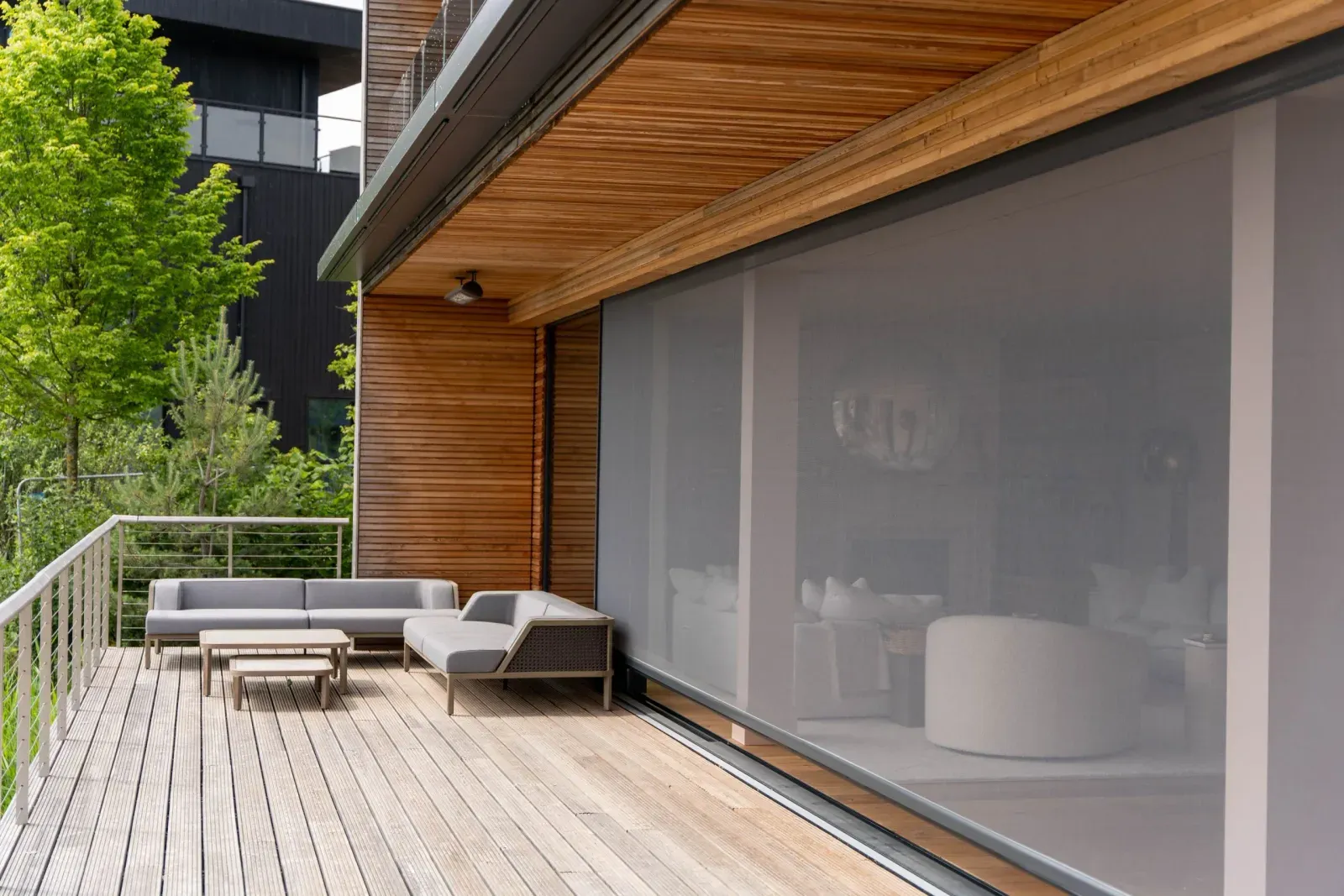 Executive outdoor screens drawn across wide sliding doors on a modern timber-clad home with a deck