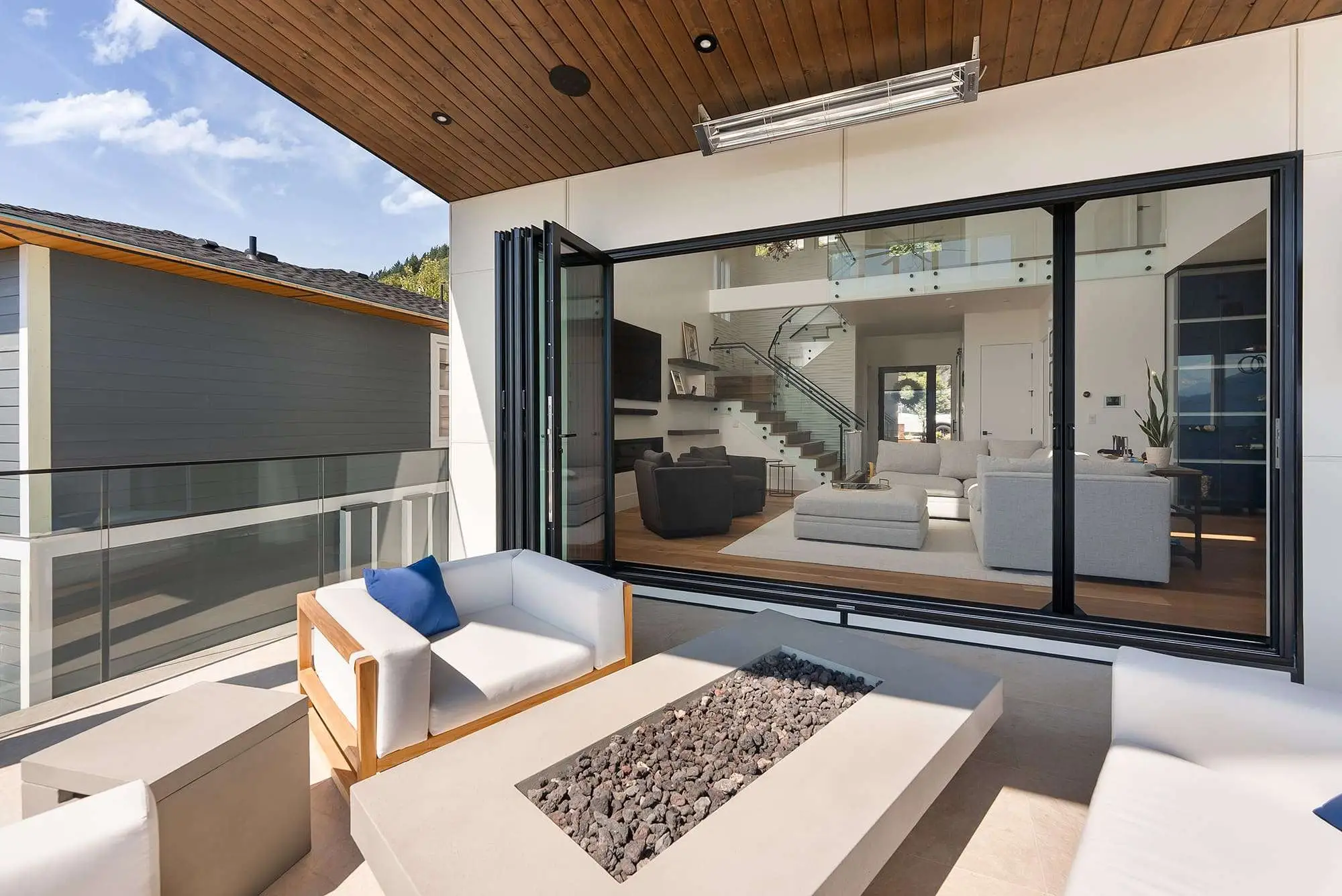 A modern New Zealand home's outdoor living terrace opening to an open-plan lounge through wide doors