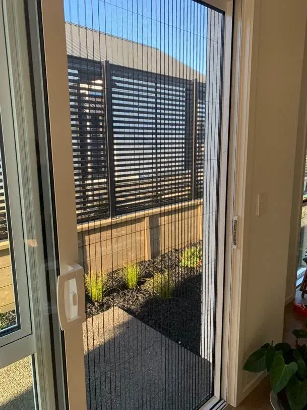 A black pleated retractable door screen drawn across a doorway, opening onto a landscaped courtyard