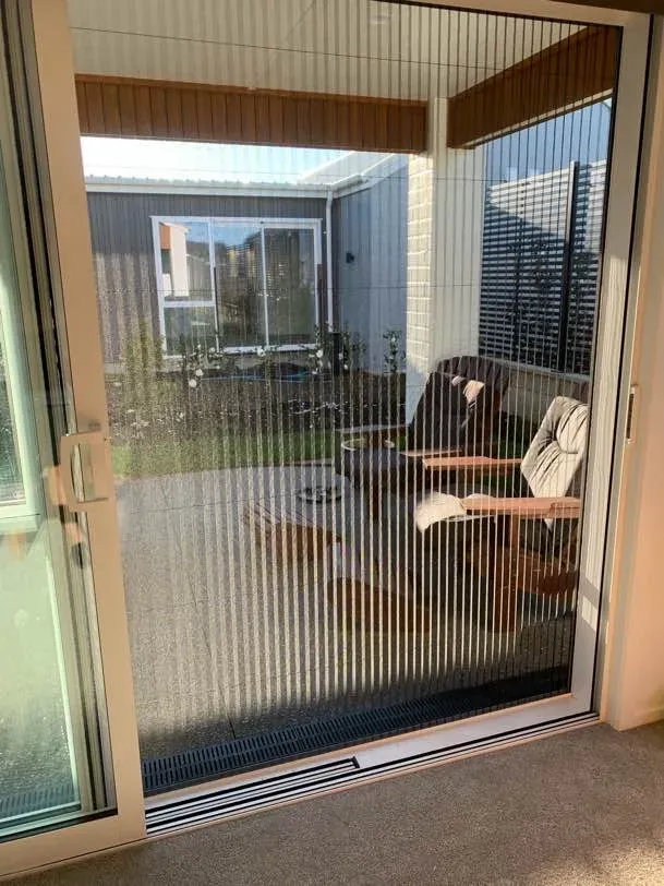 A pleated retractable door screen across a slider, looking out to a sunny courtyard with outdoor seating