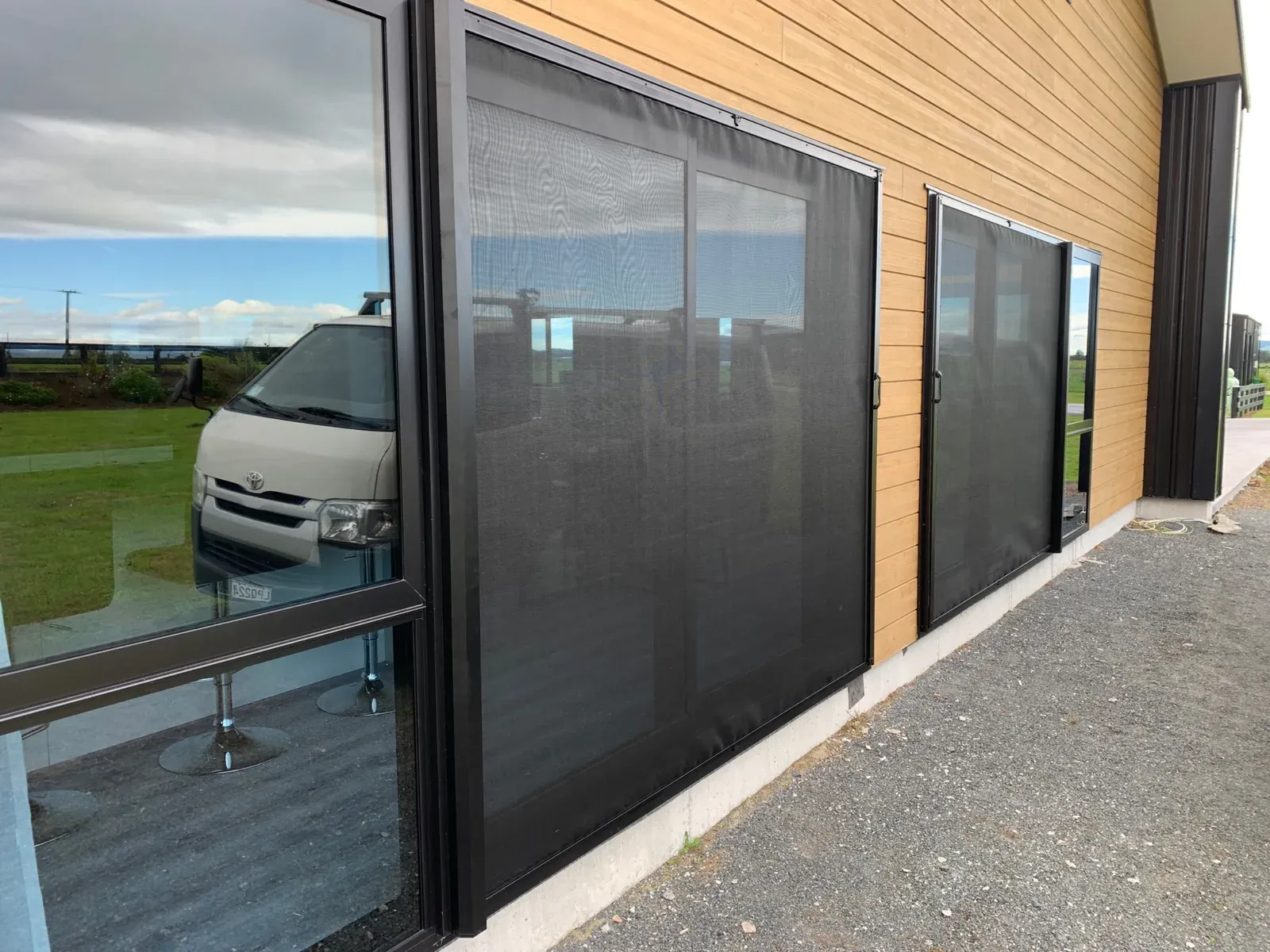 Two wide black retractable screens drawn across the glazed openings of a timber-clad rural building