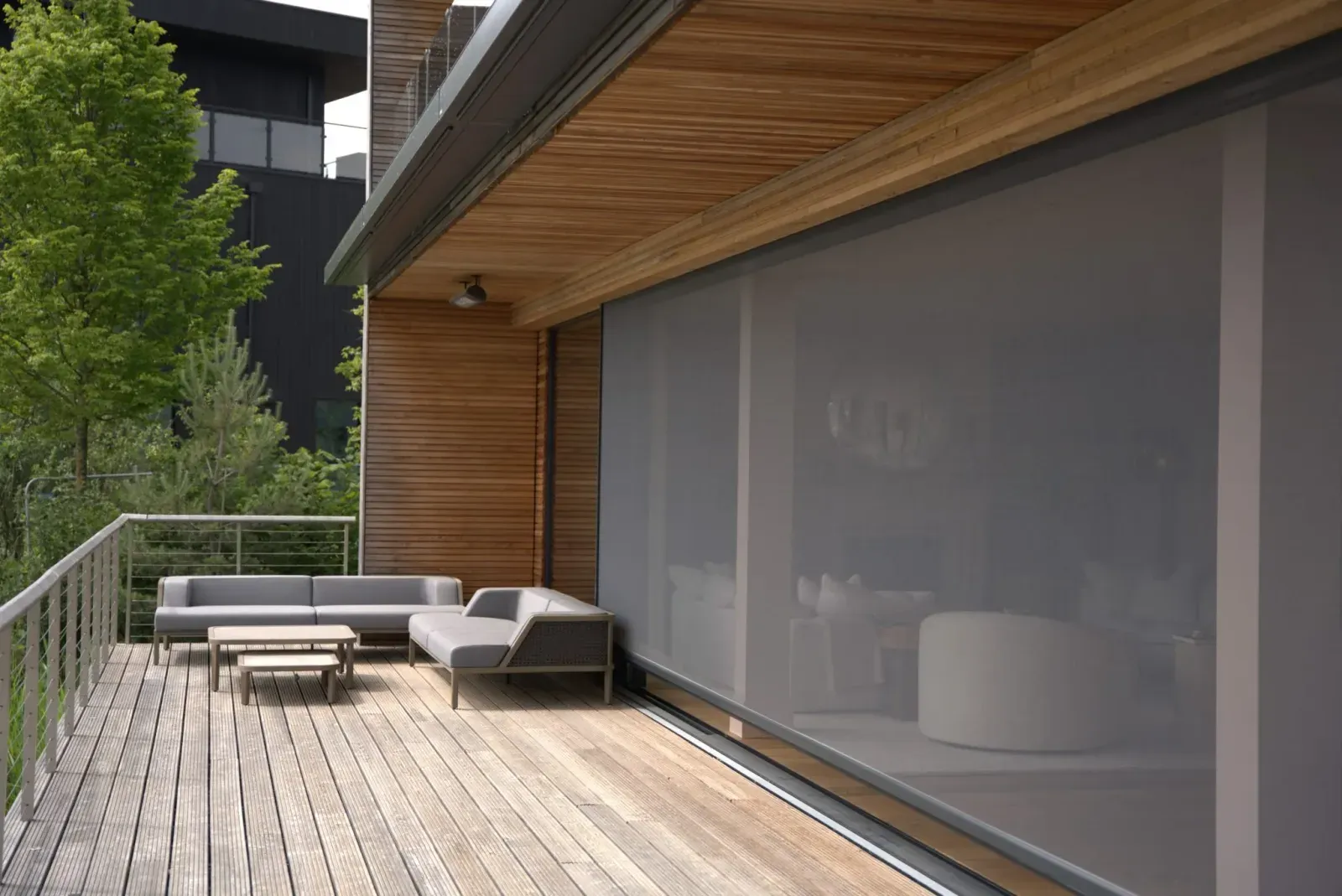 An Executive outdoor screen drawn down beside a timber-clad covered deck with outdoor furniture and trees beyond