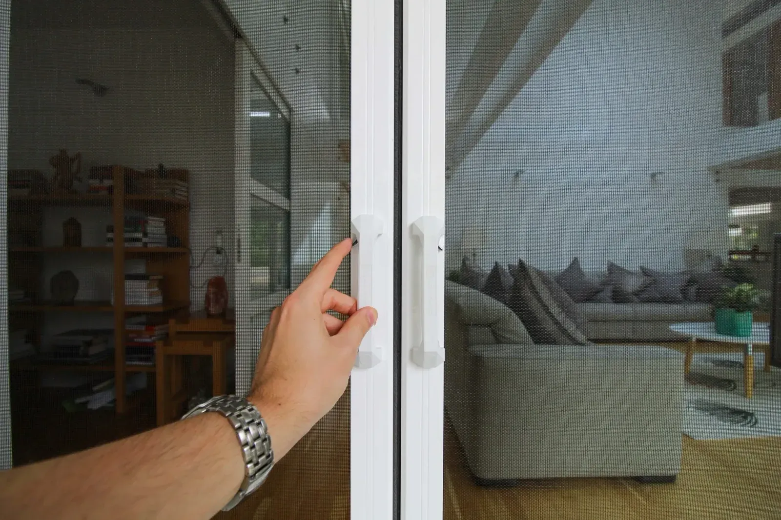 A hand releasing the centre latch where two retractable Wall Screen panels meet across a doorway