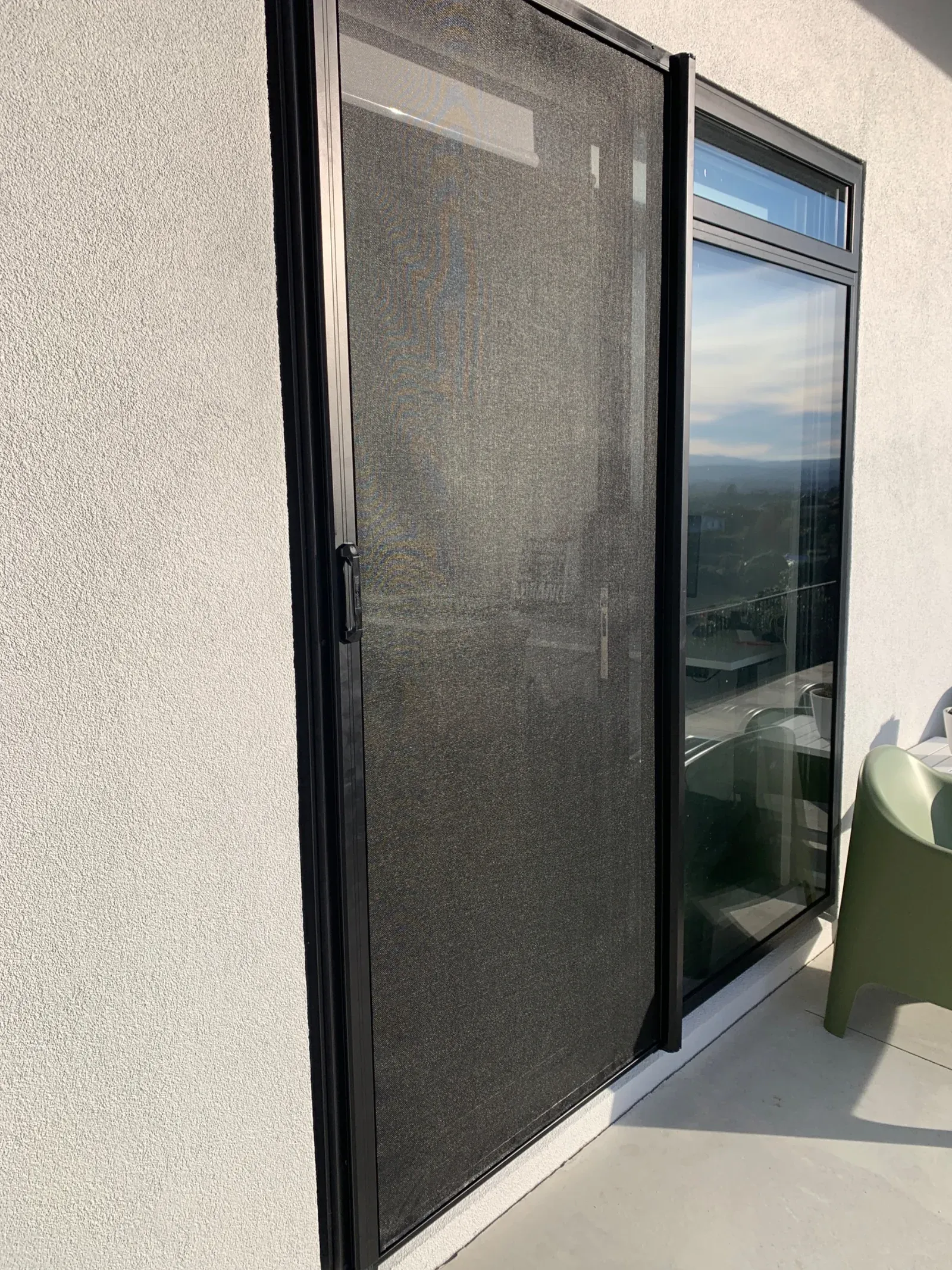 Black retractable MeshLock screen across a sliding door on an elevated home, overlooking a valley and township