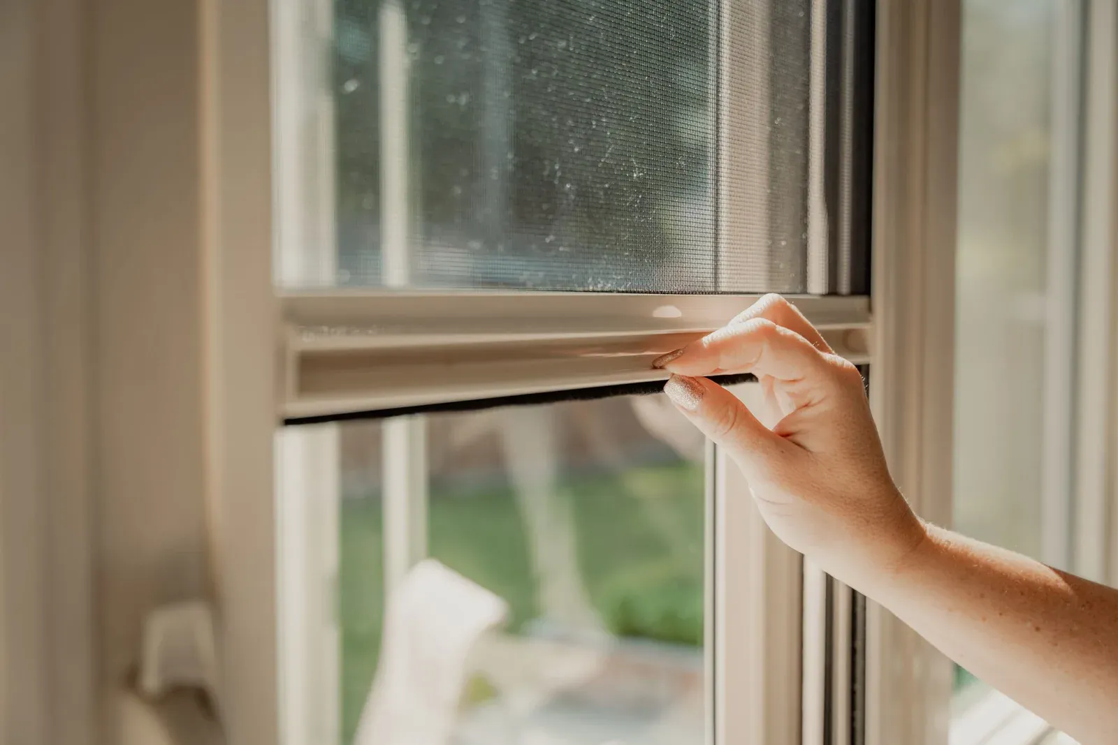 A hand drawing a retractable Serene window screen down by its bottom bar
