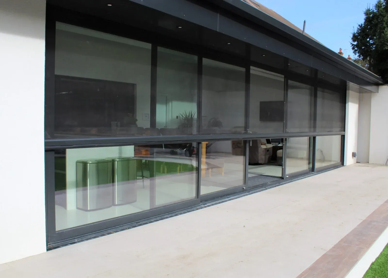 Executive outdoor screens drawn down across wide dark-framed stacking doors on a rendered home with a paved patio