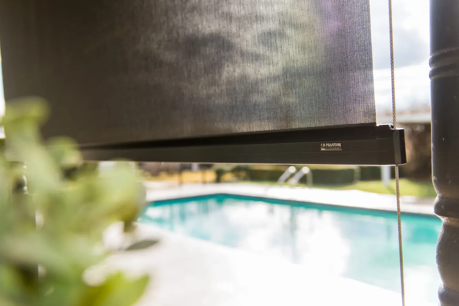 Close-up of a Phantom outdoor blind branded bottom bar and cable guide above a swimming pool