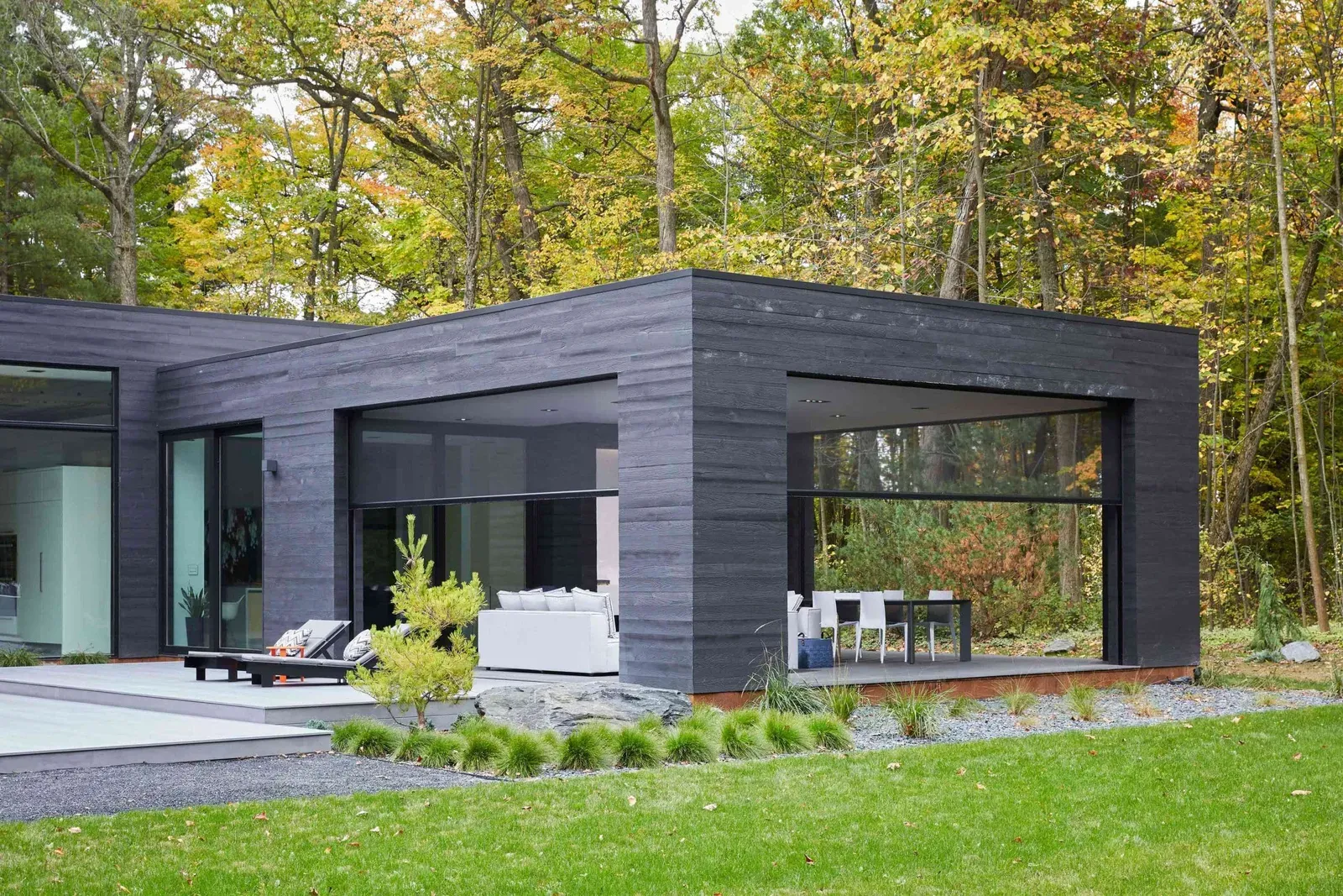 Executive outdoor screens on a black timber-clad architectural home opening to a lawn and trees