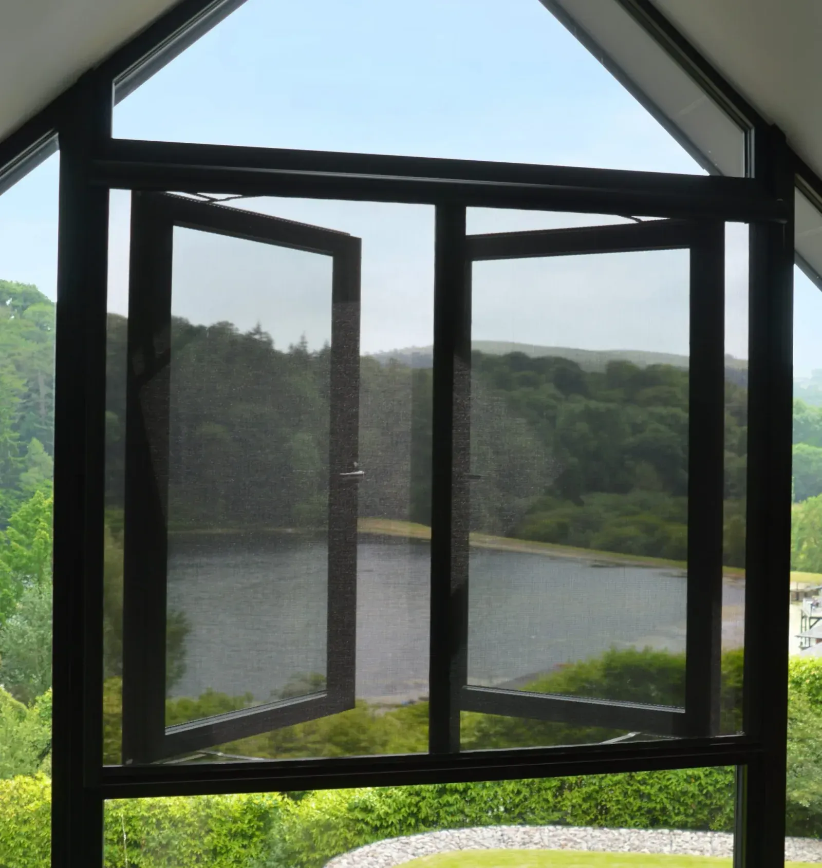 A retractable Serene window screen drawn down over a pair of outward-opening windows, a lake and bush hills beyond