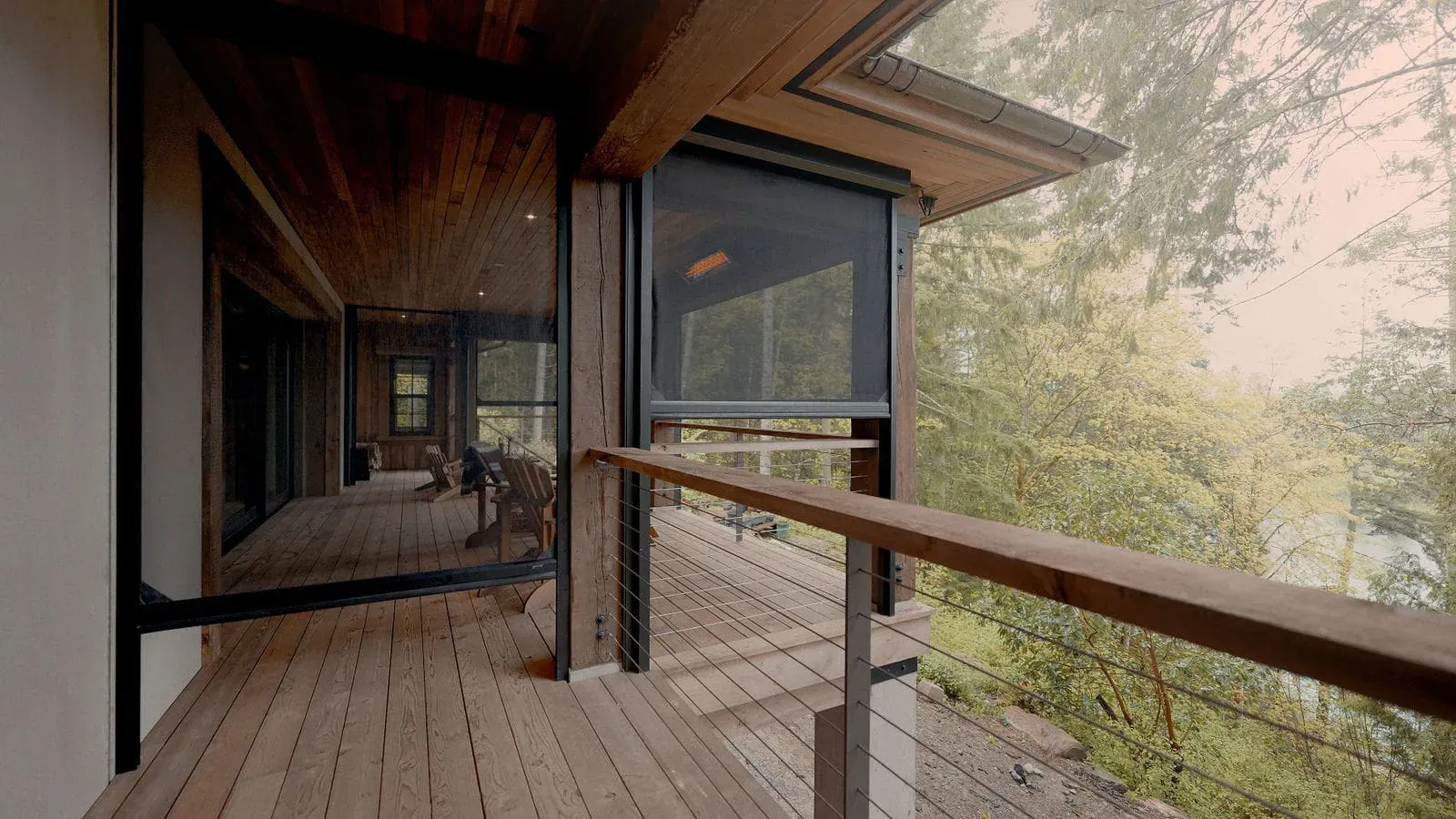 An Executive outdoor screen drawn down over a cedar-clad covered deck, with bush and water beyond