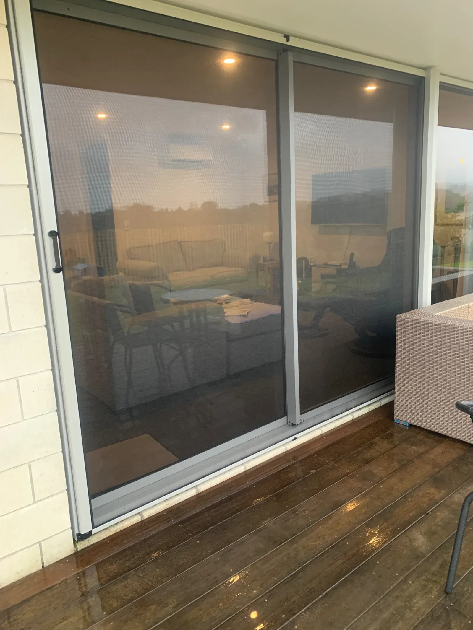 Two retractable screens meeting in the middle of a wide sliding door on a covered timber deck