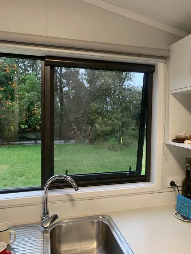 Black retractable insect screen drawn across half of the kitchen window above the sink, lawn and bush garden beyond