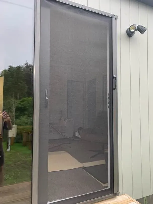 A grey retractable mesh screen door fitted across a deck doorway of a modern rural home