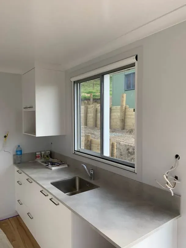 Retractable insect screen rolled into its slim top cassette above a kitchen sliding window and benchtop