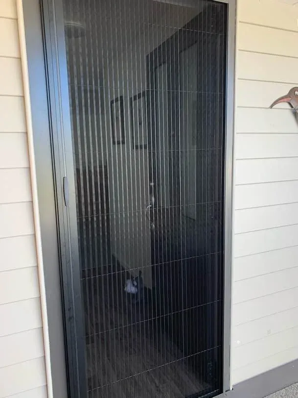 Brio pleated screen drawn across the front door of a cream weatherboard home, a small dog waiting in the hallway behind the mesh