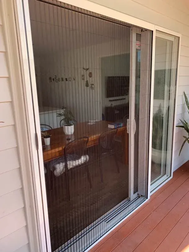 Brio pleated screen drawn across a stacker slider, the dining table and pot plants visible through the mesh