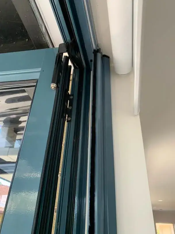 Close-up of a retractable screen track and brush seal fitted against the dark teal aluminium door joinery of a Pāpāmoa home