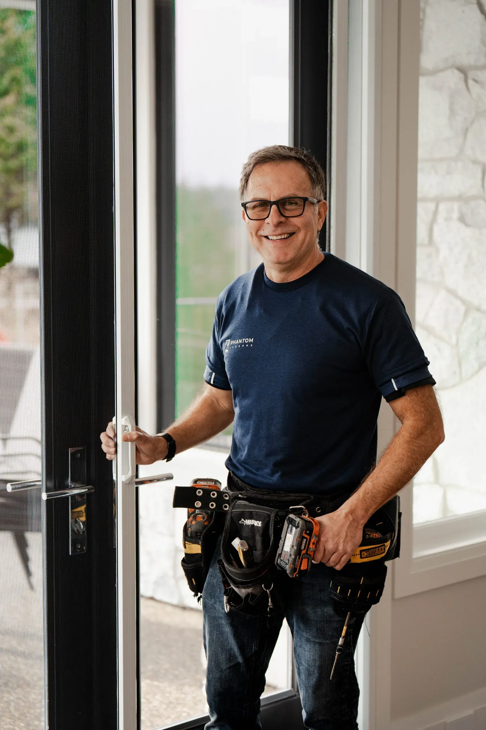 A Phantom installer in uniform, tool belt on, fitting a retractable screen at a glass door