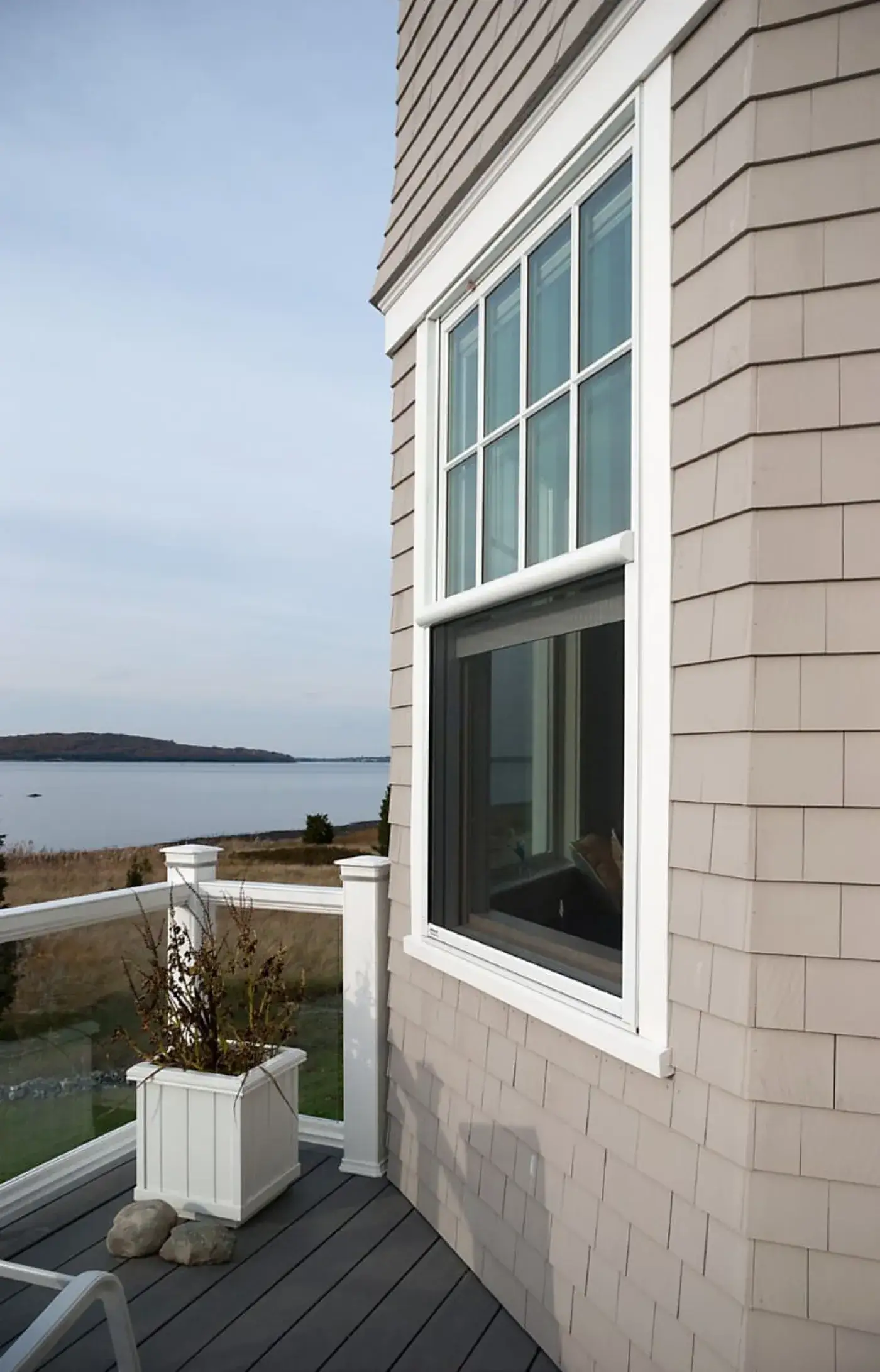 A retractable insect screen pulled down over the open lower half of a window, on a deck overlooking a calm harbour