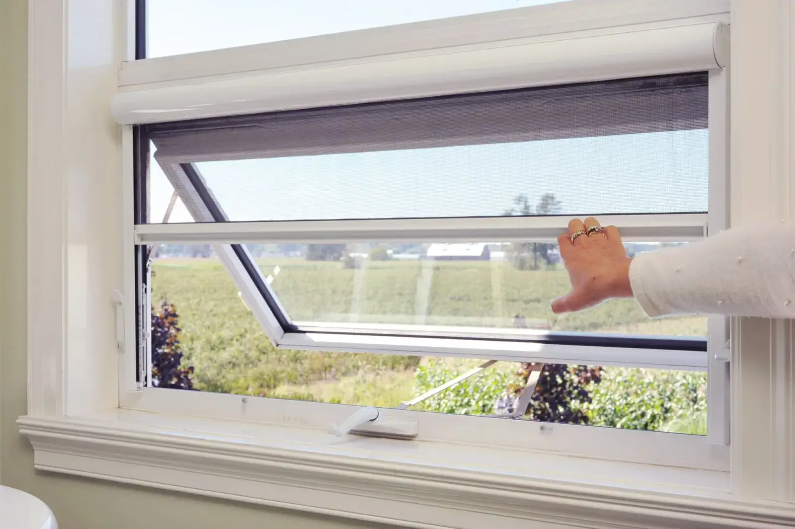 A hand drawing down a Serene retractable insect screen over an open awning window