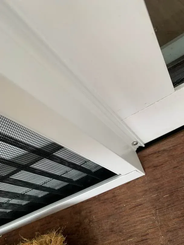 Close-up of the low threshold ramp of a pleated screen door where it meets the timber deck