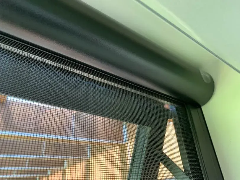 Close-up of a black Serene cassette and insect mesh drawn down over a window, brick home beyond