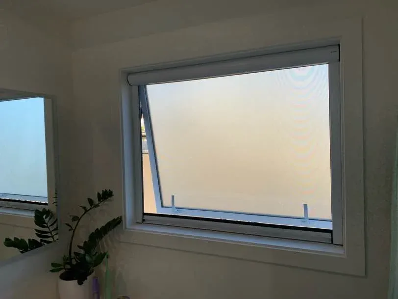 A white retractable insect screen cassette fitted above an awning bathroom window with obscure glass