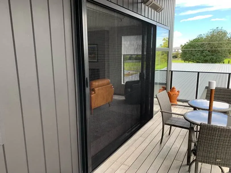 Black pleated stacking screen door drawn across a patio sliding door on a sunny Tauranga deck