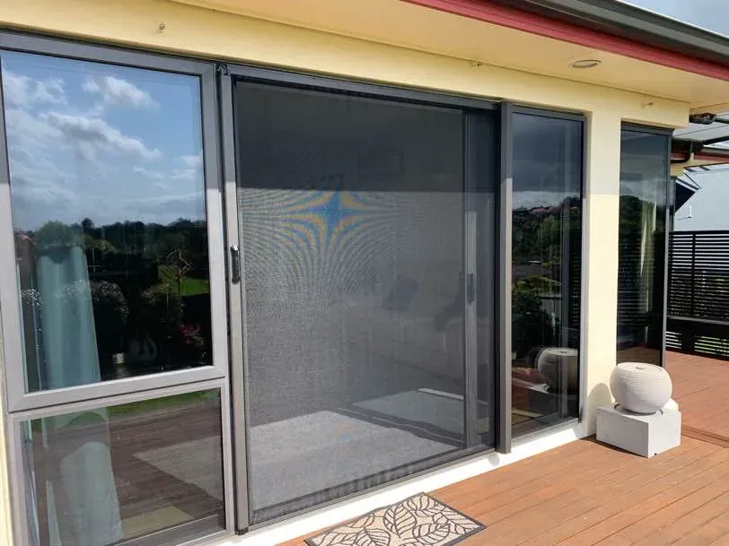 Black retractable insect screen closed across wide sliding patio doors on a sunny elevated Bay of Plenty deck
