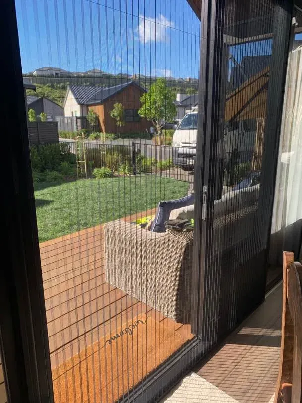 View from inside through a black pleated retractable screen door to a deck and landscaped garden