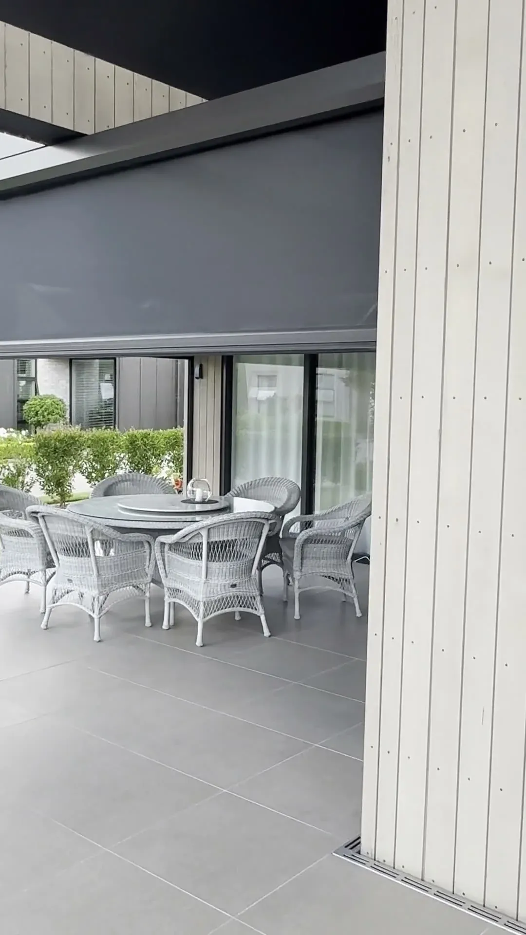 A motorised Executive screen part-lowered to enclose a covered patio with outdoor furniture