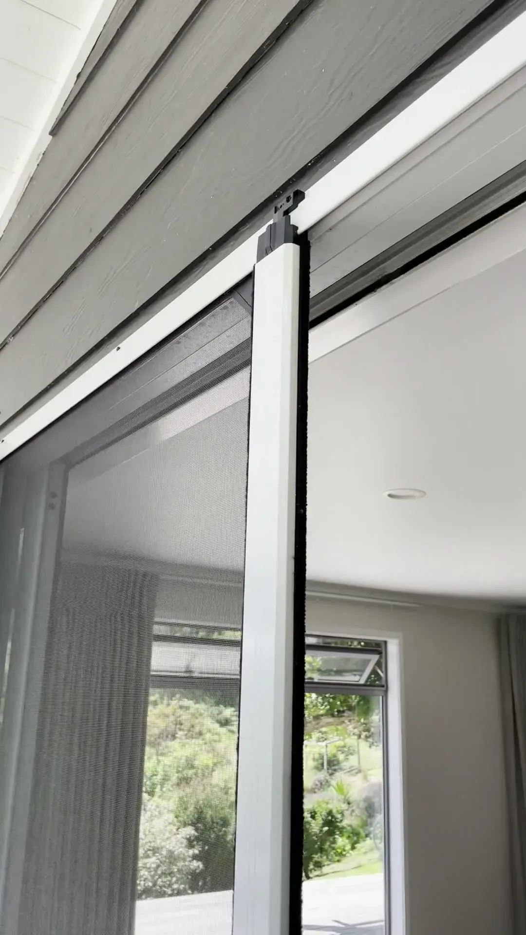 A retractable Wall Screen part-drawn across a stacker slider opening onto a deck