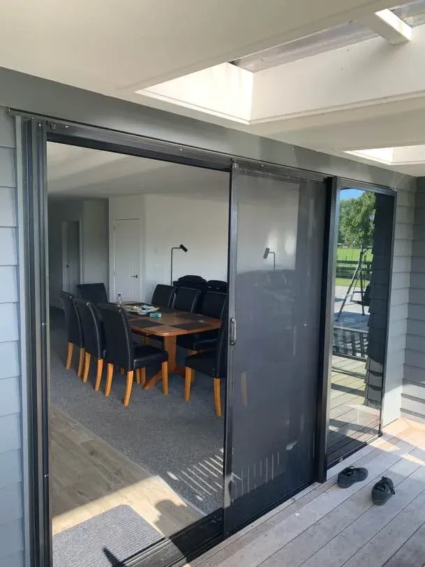 A wide retractable mesh screen drawn across a large slider, opening a sunlit dining room onto a deck