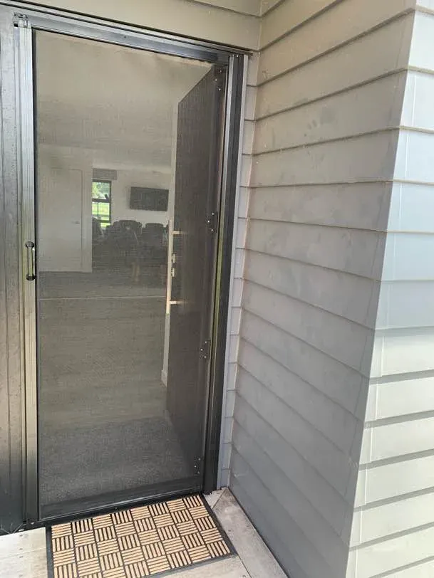 A retractable insect screen door at a weatherboard home's entry, mesh drawn across the open doorway