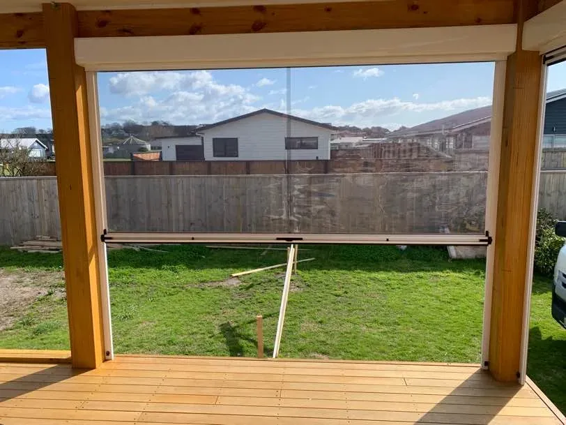 Clear PVC Ziptrak blind half lowered on a covered timber deck, showing the crystal-clear panel and bottom rail