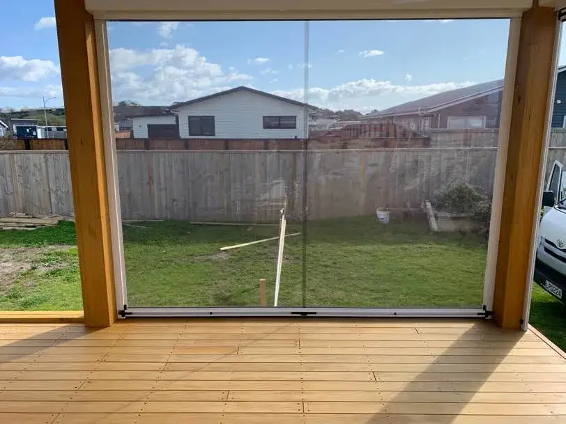 Clear PVC Ziptrak blind fully lowered to enclose a covered timber deck, keeping the lawn view