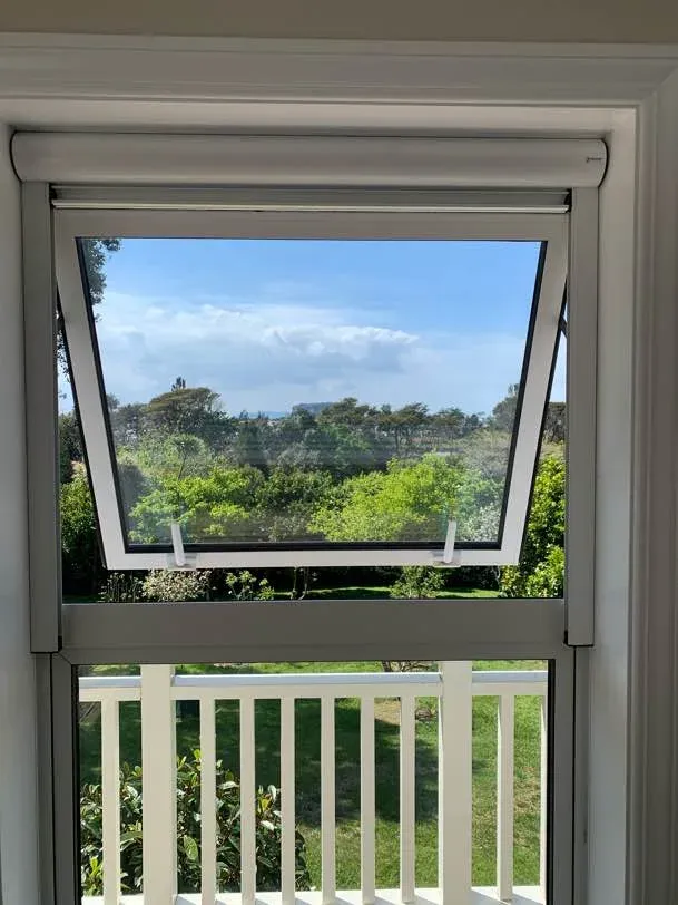 An awning window fitted with a white retractable insect screen, open to a sunny garden and deck