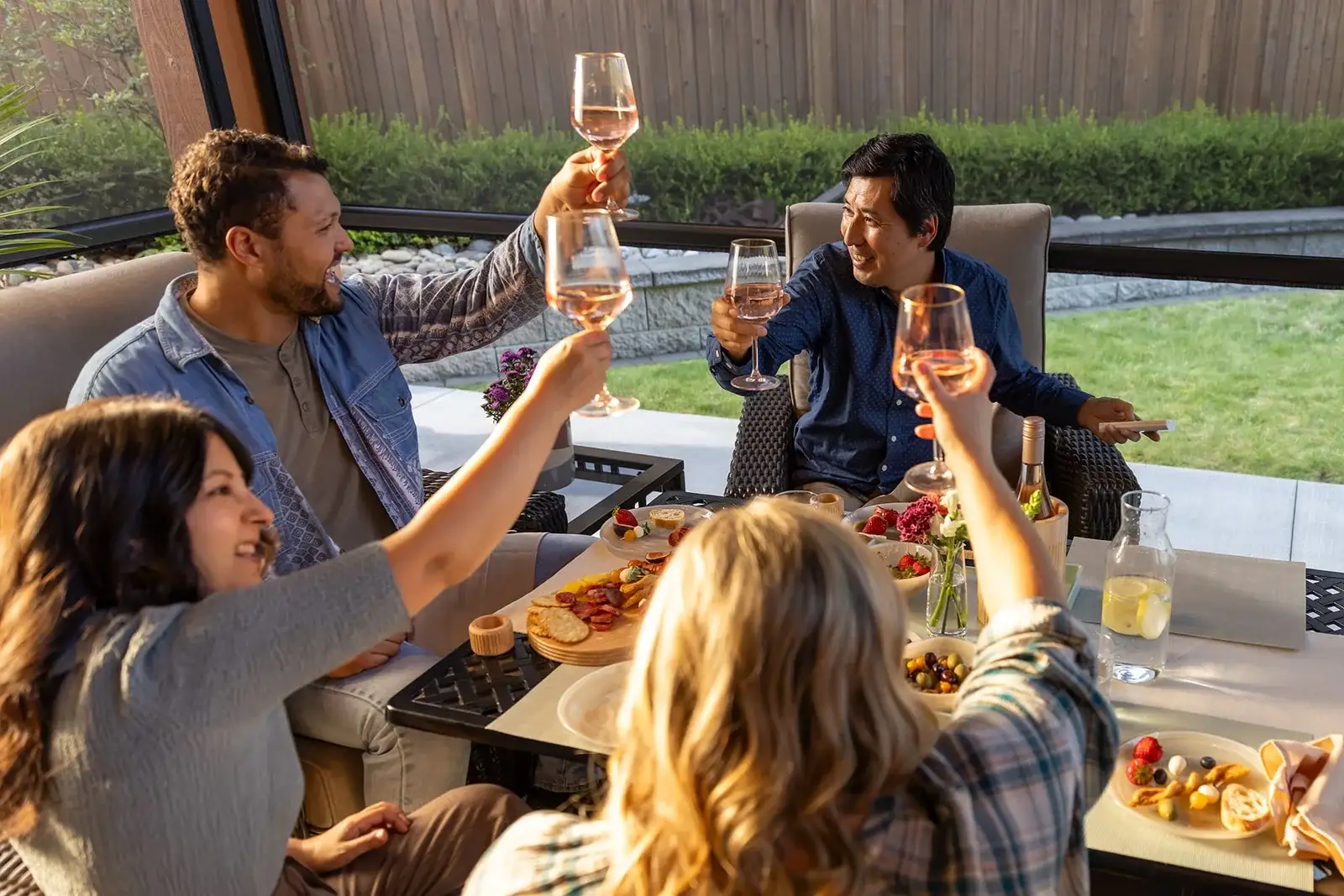 Friends dining on a covered patio enclosed by a Phantom Executive outdoor screen, the garden visible through the mesh